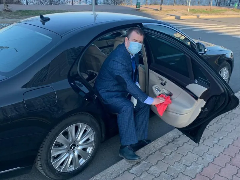 Chauffeur in a suit wiping down the door of a black Mercedes